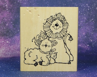 May include: A wooden rubber stamp with a black and white illustration of a lion and a lamb. The lion is wearing a frilly collar and the lamb is wearing a bow.