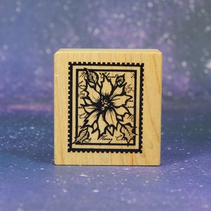 Op de afbeelding: Houten stempel met een zwart-witte illustratie van een kerstster in een decoratief kader. De tekst "Merry Christmas" is zichtbaar in het kader.