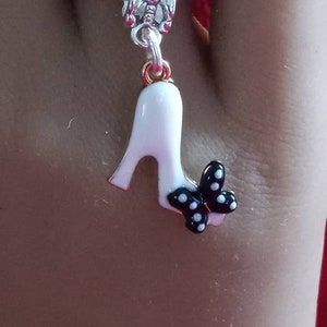 May include: A silver ring with a white shoe charm with a black and white polka dot bow. The ring is on a finger.