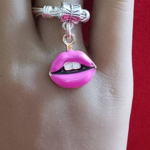 May include: A silver ring with a pink lips charm. The ring is on a finger.