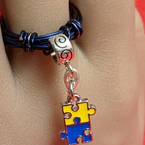Two little puzzle pieces joined together that are bright yellow and royal blue. Deep blue wired band which accents this charm ring.