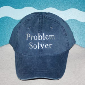 May include: A dark blue baseball cap with the words "Problem Solver" embroidered in white on the front.