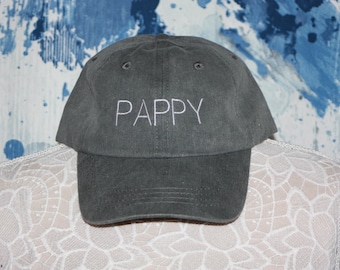 May include: A gray baseball cap with the word "PAPPY" embroidered in white. The hat has a curved brim and a classic six-panel design. The cap is displayed on a mannequin.