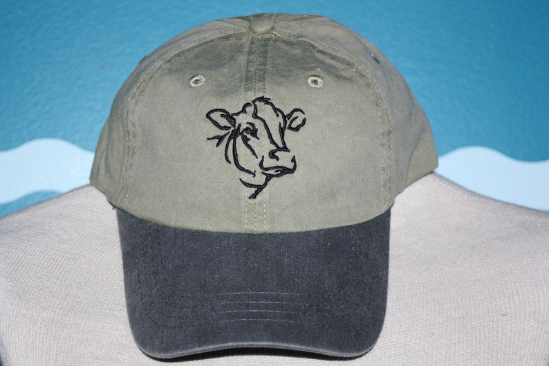 May include: A green and black baseball cap with a black embroidered cow head design.