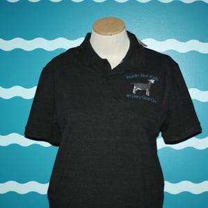 K&ouml;nnte beinhalten: Schwarzes Poloshirt mit einem wei&szlig;en gestickten Ziegenbock und dem Text "Nuthin But Kids 4-H Dairy Goat Club".