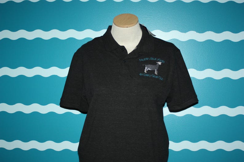 K&ouml;nnte beinhalten: Schwarzes Poloshirt mit einem wei&szlig;en gestickten Ziegenbock und dem Text "Nuthin But Kids 4-H Dairy Goat Club".