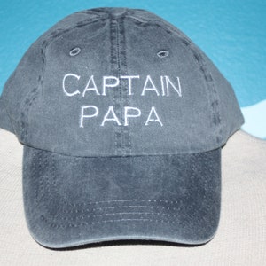 May include: A dark gray baseball cap with white embroidered text that reads "CAPTAIN PAPA".
