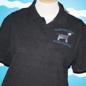 K&ouml;nnte beinhalten: Ein dunkelgraues Poloshirt mit einem gestickten Logo, auf dem "Nutr'n But Kids 4H Dairy Goat Qlt" steht und eine schwarz-wei&szlig;e Ziege abgebildet ist.