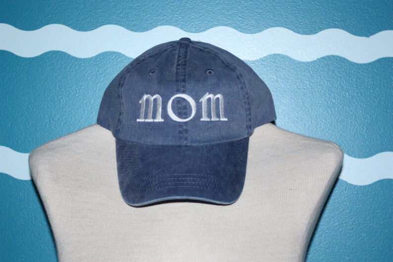 Puede incluir: Una gorra de b&eacute;isbol de mezclilla azul con bordado blanco que dice "MOM".
