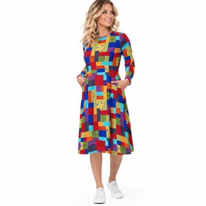 May include: A long-sleeved midi dress featuring a vibrant patchwork pattern of rectangular blocks in primary colors including red, blue, yellow, and green. The dress has a round neckline, a fitted bodice, a flared skirt, and visible side pockets.