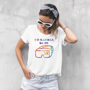 Może przedstawiać: Biała koszulka z grafiką przedstawiającą kolorowy zestaw VR i tekstem "I'd rather be in VR".