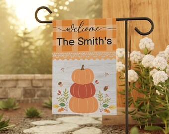 Può includere: Una bandiera da giardino di benvenuto con una pila di zucche, foglie e ghiande. La bandiera è arancione e bianca con il testo "welcome The Smith's".