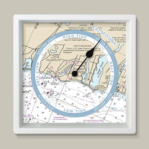 May include: A square wall clock with a white frame displays a nautical chart of Falmouth, Massachusetts. A blue tide dial indicates high and low tide times. Black clock hands show the time. The clock is a decorative item.