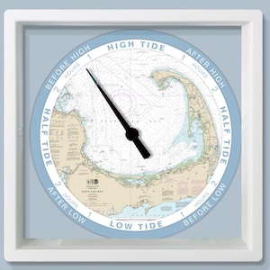 May include: A square, white-framed tide clock with a light blue face. The clock face features a nautical chart of Cape Cod, with black clock hands indicating the tide's position. Text around the perimeter reads "High Tide," "Low Tide," and "Half Tide."