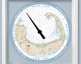 May include: A square, white-framed tide clock with a light blue face. The clock face features a nautical chart of Cape Cod, with black clock hands indicating the tide's position. Text around the perimeter reads "High Tide," "Low Tide," and "Half Tide."