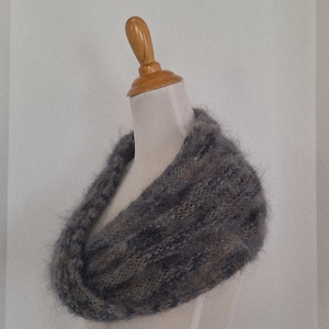 May include: A gray and brown knitted cowl scarf displayed on a mannequin. The scarf is made of a soft, textured yarn and has a looped design. The color palette includes shades of gray, brown, and a hint of beige.
