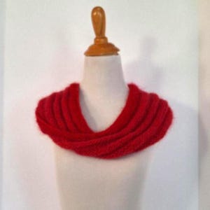 May include: A vibrant red knitted infinity scarf displayed on a mannequin. The scarf is made of a thick, textured yarn and is designed to be worn around the neck. The bright red color makes it a bold fashion accessory.