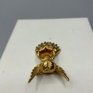 Pu&ograve; includere: Un fermaglio a forma di angelo dorato con un'aureola tempestata di cristalli e ali spiegate.