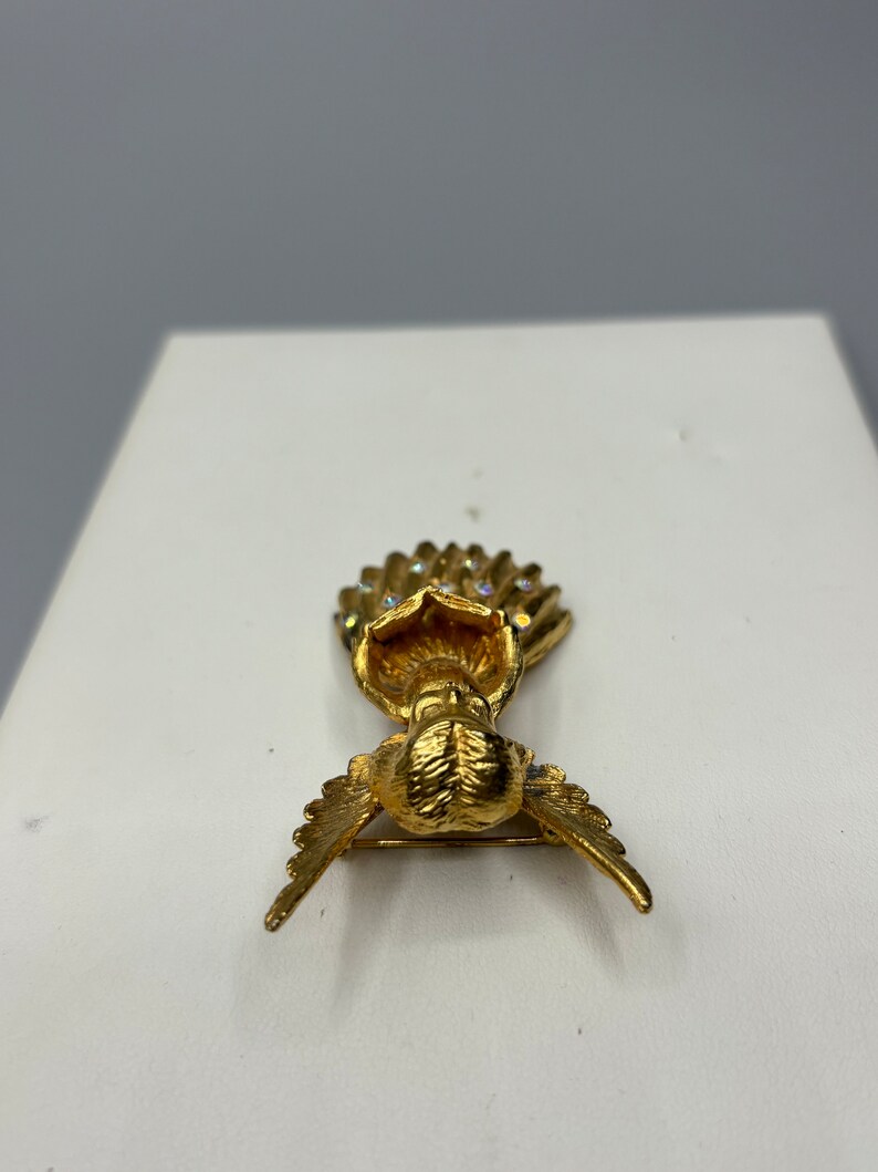 Pu&ograve; includere: Un fermaglio a forma di angelo dorato con un'aureola tempestata di cristalli e ali spiegate.