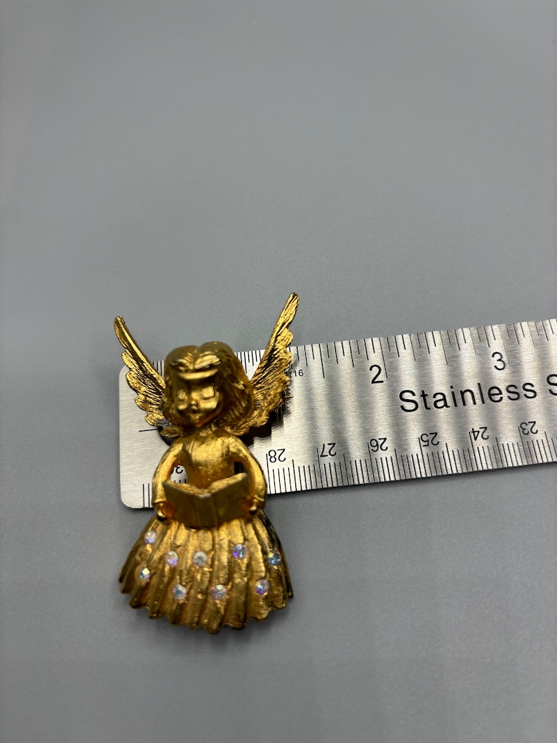 Pu&ograve; includere: Figurina di angelo dorata che tiene un libro con un vestito scintillante. L'angelo &egrave; alto circa 5 cm.