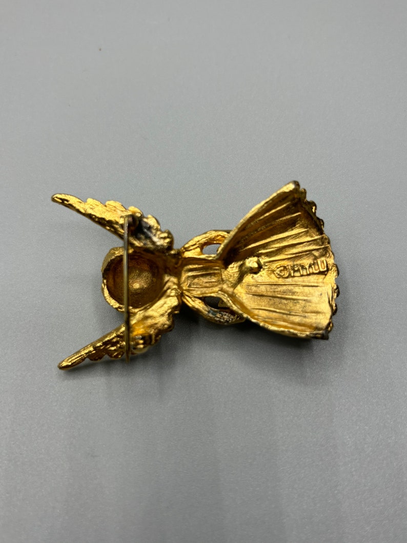 Pu&ograve; includere: Spilla a forma di angelo dorata con un design dettagliato. Il retro della spilla ha uno spillo e una piccola iscrizione che recita "CR1110".