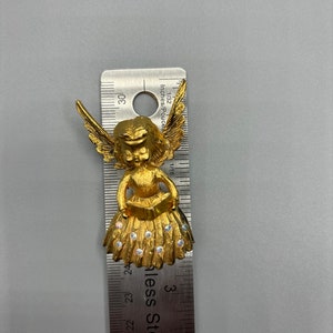 Pu&ograve; includere: Figurina di angelo dorata con ali, che tiene un libro e indossa un vestito con strass. La figurina &egrave; alta circa 2,5 cm.