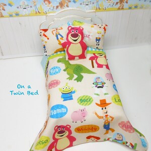 May include: Toy Story dollhouse bedding set with a white twin bed, a white and blue checkered pillow, a red pillow with a bear face, and a white comforter with a colorful Toy Story character print. The comforter features characters like Woody, Buzz Lightyear, Rex, and Hamm.