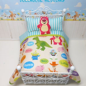 May include: Toy Story dollhouse bedding set with a white metal bed frame and a white, blue, and green striped pillow. The bedding features a cream background with colorful images of Toy Story characters, including Buzz Lightyear, Woody, Rex, and Hamm.