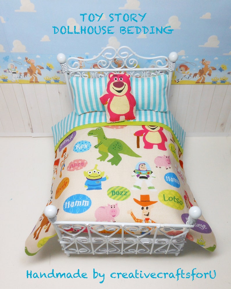 May include: Toy Story dollhouse bedding set with a white metal bed frame and a white, blue, and green striped pillow. The bedding features a cream background with colorful images of Toy Story characters, including Buzz Lightyear, Woody, Rex, and Hamm.