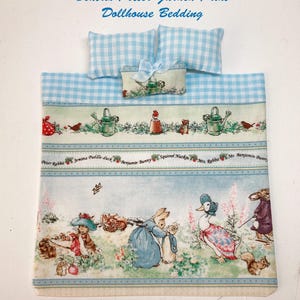May include: Dollhouse bedding set with a Beatrix Potter Garden Print. The set includes a blue and white gingham patterned comforter, two pillows, and a small pillow with a bow. The comforter features illustrations of Peter Rabbit and other characters. Handmade in the USA.
