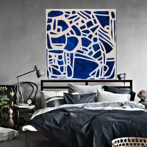 May include: Abstract art print with a white geometric design on a dark blue background. The print is framed and hanging above a bed with black bedding.