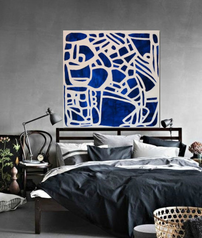 May include: Abstract art print with a white geometric design on a dark blue background. The print is framed and hanging above a bed with black bedding.