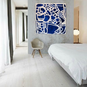 May include: A white bedroom with a white bed, a white chair, and a large blue and white abstract painting on the wall.