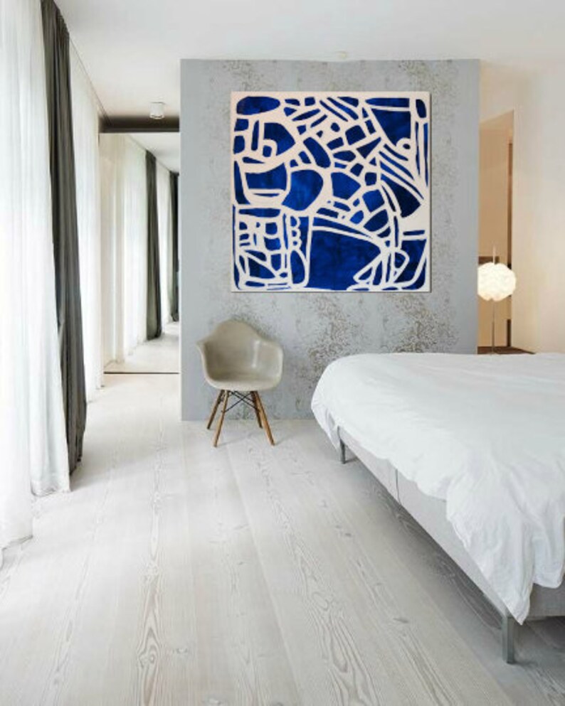May include: A white bedroom with a white bed, a white chair, and a large blue and white abstract painting on the wall.