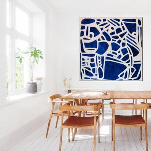 May include: Abstract painting with a white geometric design on a deep blue background. The painting is framed and hanging on a white wall in a dining room.