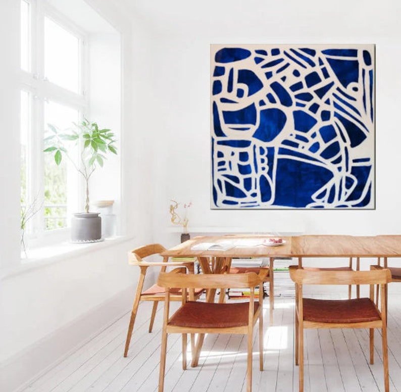 May include: Abstract painting with a white geometric design on a deep blue background. The painting is framed and hanging on a white wall in a dining room.