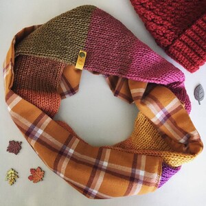 May include: A knitted infinity scarf with a plaid fabric lining. The scarf is made in a variety of colors, including pink, brown, and mustard yellow.