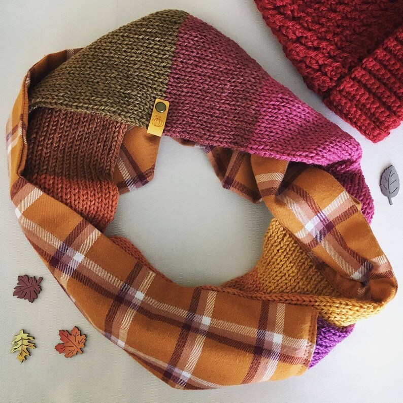 May include: A knitted infinity scarf with a plaid fabric lining. The scarf is made in a variety of colors, including pink, brown, and mustard yellow.