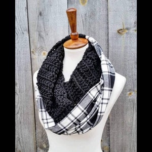 May include: A black crocheted infinity scarf with a white and black plaid lining. The scarf is displayed on a wooden mannequin.
