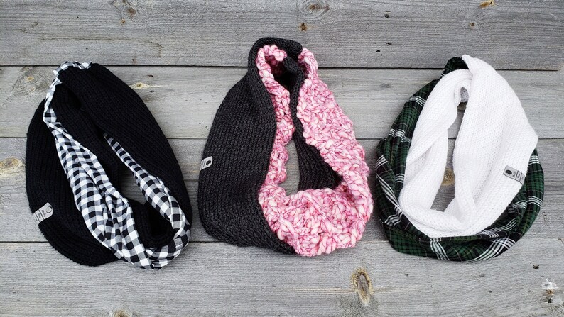 May include: Three reversible infinity scarves. The first scarf is black with a black and white checkered pattern on the reverse side. The second scarf is gray on one side and pink on the other. The third scarf is green and white plaid on one side and white on the other.