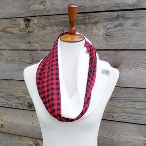 May include: A white infinity scarf with a red and black buffalo plaid pattern on one side. The scarf is displayed on a white mannequin.