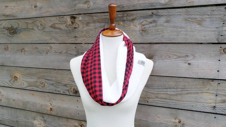 May include: A white infinity scarf with a red and black buffalo plaid pattern on one side. The scarf is displayed on a white mannequin.