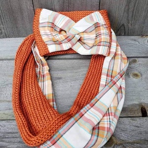 May include: A knitted infinity scarf with a plaid fabric lining. The scarf is a burnt orange color and the plaid fabric is white with orange, pink, and blue stripes.