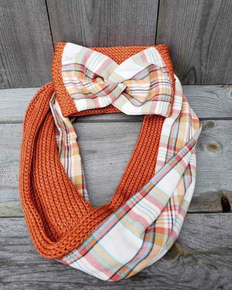 May include: A knitted infinity scarf with a plaid fabric lining. The scarf is a burnt orange color and the plaid fabric is white with orange, pink, and blue stripes.