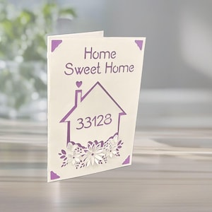 May include: A cream-colored card with the words "Home Sweet Home" in purple script. A purple house graphic with the number "33128" is below the text. The card is decorated with purple corner accents and floral cutouts.