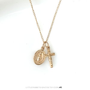 May include: Gold chain necklace with two charms: a round, oval-shaped pendant depicting the Virgin Mary and a small cross with a figure of Jesus Christ.