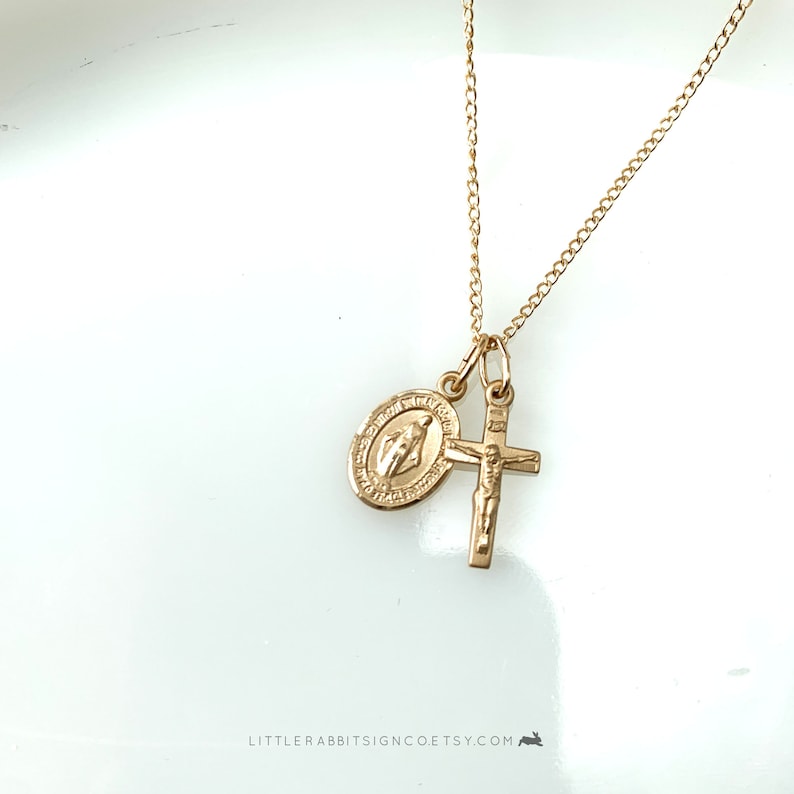 May include: Gold chain necklace with a gold cross and a gold oval pendant featuring the Virgin Mary.