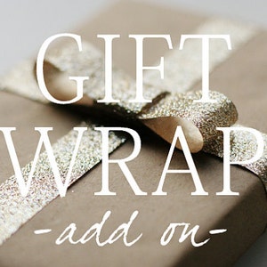 Pode incluir: Papel de embrulho marrom com uma fita dourada e o texto "GIFT WRAP - add on -" impresso nele.