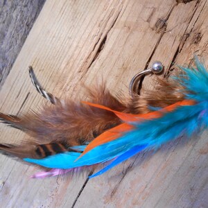 May include: A turquoise, orange, and brown feather earring with a silver hoop and a small bead.