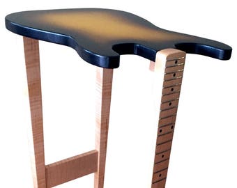 May include: A wooden guitar-shaped end table with a natural wood finish and a black top. The table has a guitar neck extending from the top, with a fretboard and tuning pegs.